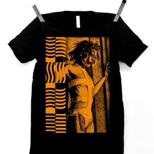 May include: A black short-sleeved t-shirt featuring a graphic print in orange. The design displays a stylised figure in a cutout outfit next to a vertical column of stacked, curved, and straight horizontal lines, creating a high-contrast visual.