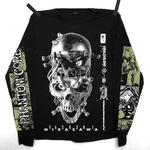 Könnte beinhalten: Ein schwarzes Langarmshirt mit einer großen, detaillierten Grafik eines mechanischen Schädels auf der Vorderseite. Der Text "PHANTOM CORE" ist auf dem linken Ärmel gedruckt, während "NYIARSAUSSAHWIA" unter dem Schädel erscheint. Die Ärmel zeigen Comic-Illustrationen.