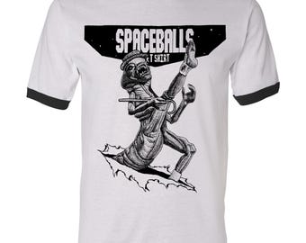 Könnte beinhalten: Weißes Ringel-T-Shirt mit schwarzem Besatz. Es zeigt eine Schwarz-Weiß-Illustration einer Kreatur, die durch eine Oberfläche bricht. Das Shirt hat den Text "SPACEBALLS T SHIRT" in einem schwarzen Rechteck.