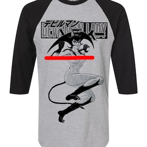 May include: A gray raglan baseball tee with black sleeves. The shirt features a black and white graphic of a female demon with the text "DEVILMAN LADY" in Japanese and English.