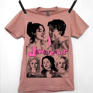 May include: A pink t-shirt featuring a black and white graphic print of a couple sharing a popsicle. The text "Jawbreaker" is printed in pink and black below the couple. Three women are pictured below the text.