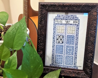 May include: A framed cross-stitch of a blue police box with the words "Police Public Call Box" on the front. The cross-stitch is in a brown frame with ornate detailing.