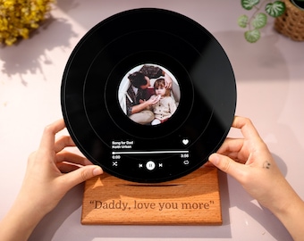 May include: A black vinyl record with a photo of a father and child. The record has a digital music player interface with the song title "Song for Dad" by Keith Urban. The record is on a wooden stand with the text "Daddy, love you more".