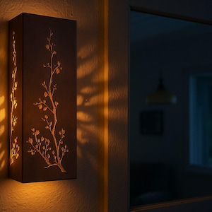 May include: A rectangular, brown wall sconce featuring a floral branch design. The sconce emits a warm, orange glow, casting patterned light onto the wall. This decorative lighting fixture is ideal for adding ambiance to any room.