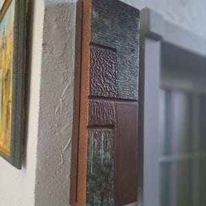 May include: A rectangular wall art piece with a geometric design. The art is made of wood and has a brown, green, and copper colour scheme.