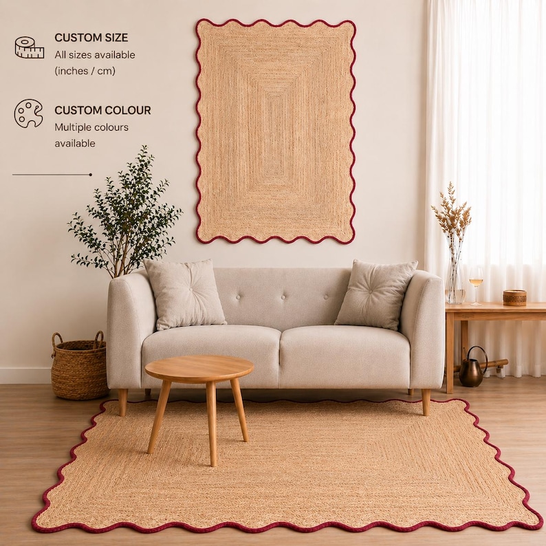 Puede incluir: Una alfombra rectangular de yute trenzado con un borde festoneado acabado en un ribete rojo oscuro. La alfombra se muestra tanto en el suelo como colgada en la pared. El texto indica que hay tama&ntilde;os y colores personalizados disponibles.