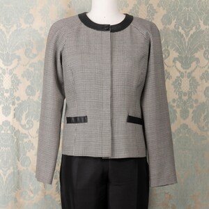 May include: A black and white houndstooth blazer with a black trim and a black button closure. The blazer is paired with black pants.