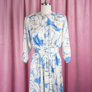 May include: A blue and white floral dress with a white belt. The dress has a long sleeve and a flowing skirt.
