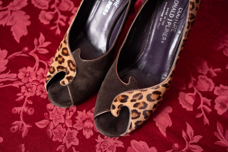 K&ouml;nnte beinhalten: Ein Paar Donald J Pliner Couture Peeptoe-Pumps mit einer Vorderseite aus dunkelbraunem Wildleder und einem Leopardenmuster-Overlay aus Kalbshaar. Das Innenfutter ist dunkelviolett mit dem Markennamen und Made in the Mountains of Italy in Wei&szlig;.