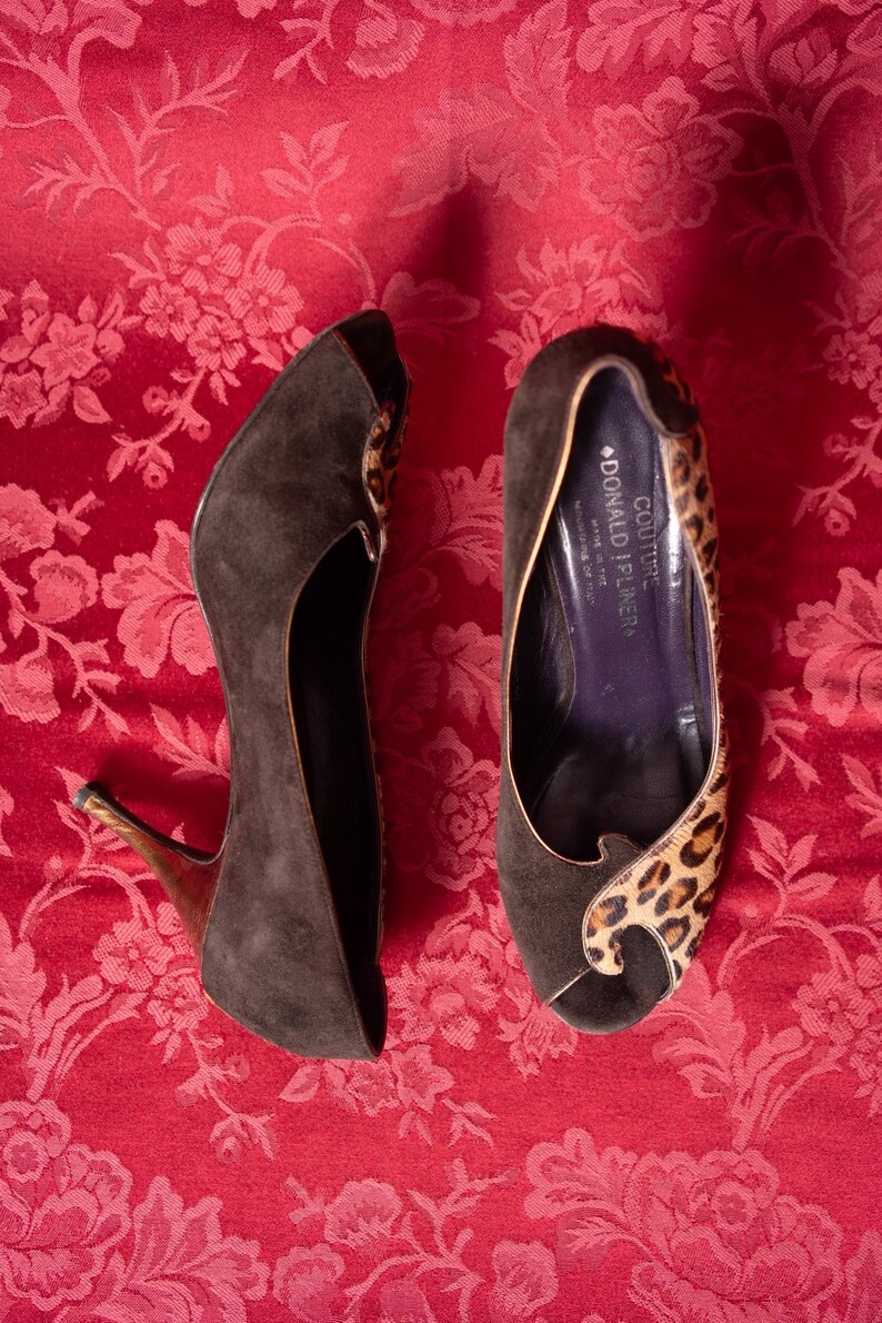 K&ouml;nnte beinhalten: Ein Paar Donald J Pliner Couture Peeptoe-Pumps aus dunkelbraunem Wildleder mit Leopardenmuster-Akzenten. Das Innere des Schuhs ist dunkelviolett und zeigt den Markennamen sowie einen Hinweis auf die Herstellung in den Bergen Italiens.