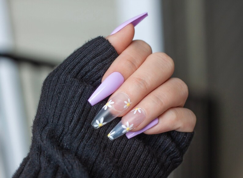 May include: Long, lavender-colored acrylic nails with clear tips decorated with white daisy flowers.