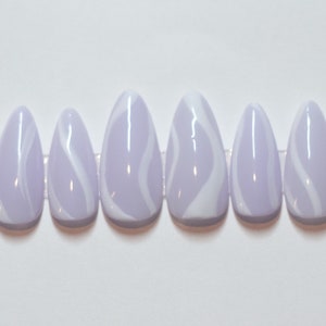 Puede incluir: Conjunto de diez u&ntilde;as postizas de color lavanda con dise&ntilde;os de remolinos blancos.