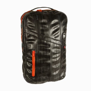 Puede incluir: Una mochila negra hecha de cámaras de bicicleta recicladas. La mochila tiene tiradores de cremallera naranja y un pequeño logotipo en la parte delantera que dice "AG".