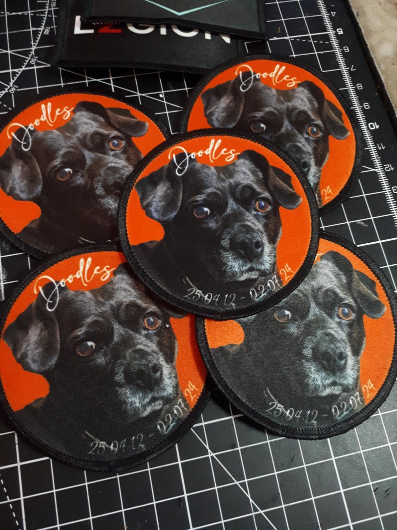 May include: A collection of five circular patches featuring a black dog with brown eyes. Each patch has an orange border and the name "Doodles" in cursive. The dates "25.04.12 - 02.07.24" are also printed on the patches.
