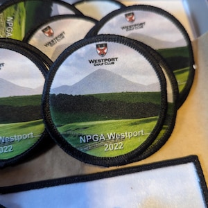 May include: A collection of round embroidered patches. Each patch features a landscape scene with a mountain, green field, and the text "NPGA Westport 2022" and "Westport Golf Club". The patches have a black border.
