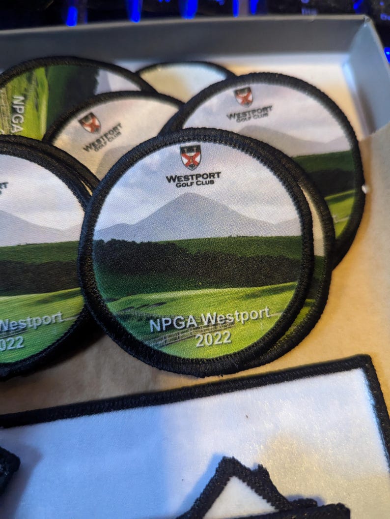 May include: A collection of round embroidered patches. Each patch features a landscape scene with a mountain, green field, and the text "NPGA Westport 2022" and "Westport Golf Club". The patches have a black border.