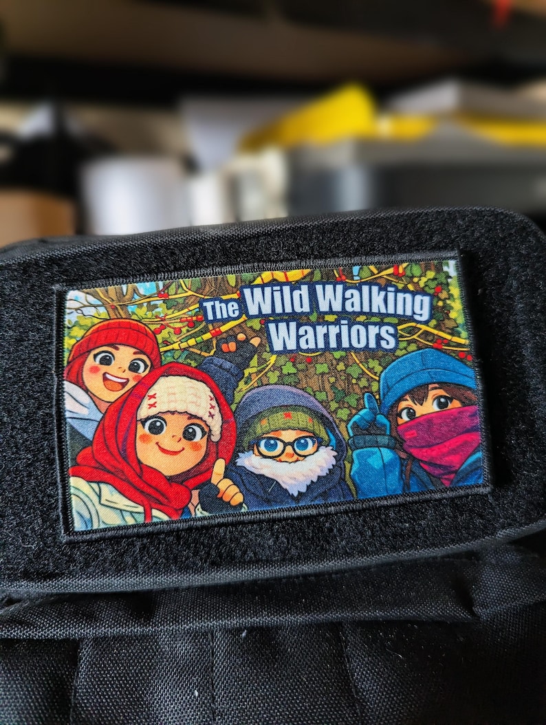 May include: A rectangular patch with the text "The Wild Walking Warriors" above a colorful cartoon illustration of four characters. The patch is bordered by black fabric with a hook and loop fastener.