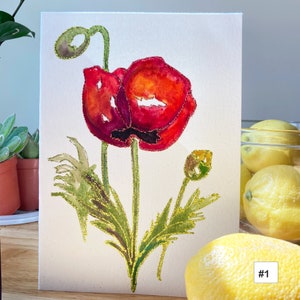 May include: Watercolor painting of a red poppy flower with gold glitter accents on the petals and stem. The flower is on a white background with green leaves.