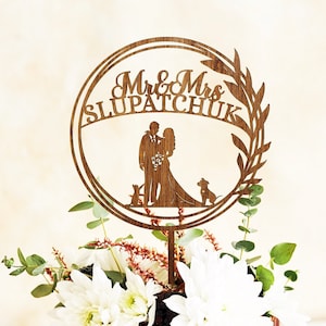 Może przedstawiać: Tort weselny z drewnianym topperem z napisem "Mr & Mrs SLUPATCHUK". Tort jest udekorowany białymi kwiatami, czekoladowymi kroplami i świeżymi jeżynami. Drewniany topper przedstawia sylwetkę pary i dwa psy.