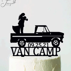 Può includere: Un cake topper nero con la silhouette di una coppia che si abbraccia su un camioncino vintage. La data "09.25.21" e le parole "VAN CAMP" sono visualizzate sotto il camion. Il topper è posto su una torta glassata bianca.