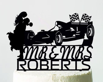 Könnte beinhalten: Ein schwarzer Tortenaufsatz mit einer Silhouette eines Paares, eines Rennwagens und karierten Flaggen. Die Worte "MR & MRS ROBERTS" sind unter dem Auto zu sehen. Der Kuchen steht auf einer weißen Tortenplatte.