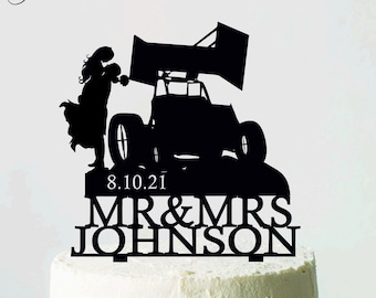 Könnte beinhalten: Ein schwarzer Tortenaufsatz mit einem Rennwagen und einem sich küssenden Paar. Der Aufsatz enthält das Datum 8.10.21 und die Namen MR & MRS JOHNSON. Der Kuchen ist weiß und steht auf einem weißen Tortenständer.