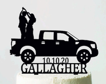 May include: Black cake topper depicting a pickup truck with a dancing couple. The date "10.10.20" and the name "Gallagher" are below the truck. The cake sits on a white cake stand, ideal for a wedding.