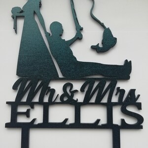 May include: Navy blue wedding cake topper featuring a bride and groom silhouette, with the groom fishing. The topper includes the text "Mr & Mrs ELLIS". The bride is holding a bouquet. The fishing rod has a fish on the end.