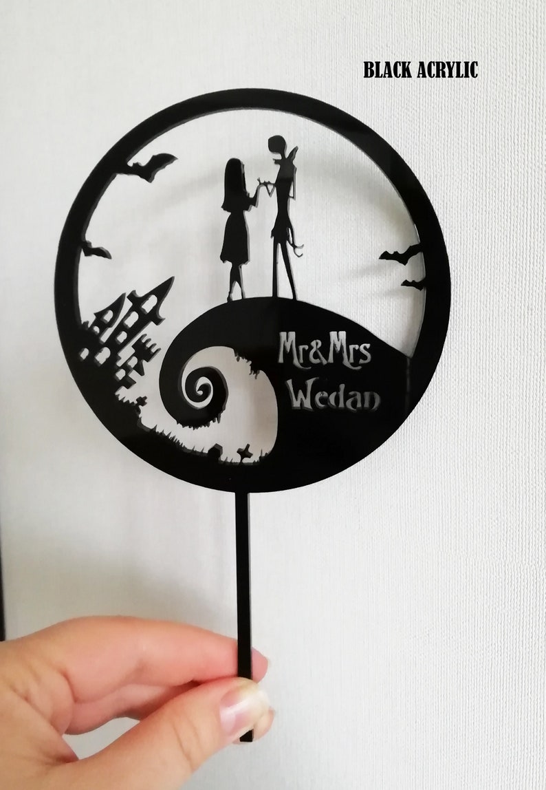 Pu&ograve; includere: Topper per torta nuziale in acrilico nero con sagome di una coppia, una casa stregata e pipistrelli. Il design include il testo "Mr & Mrs Wedan" all'interno di una cornice circolare, perfetto per un matrimonio a tema.