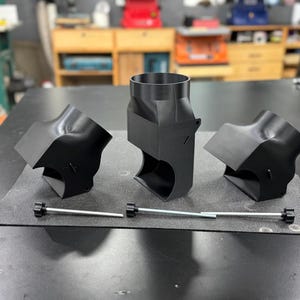 May include: Three black plastic 3D printed parts with a silver metal rod. The parts are shaped like a cylinder with a curved opening on one side.