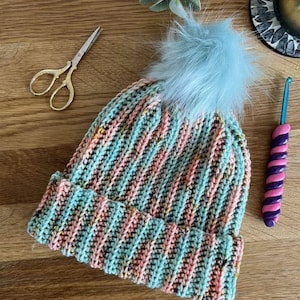 May include: A teal and pink striped crocheted beanie with a light blue faux fur pom pom.