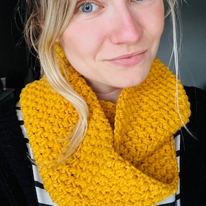 Puede incluir: Primer plano de una mujer con una bufanda infinita de crochet amarilla. La bufanda está hecha con un punto texturizado y está doblada dos veces.