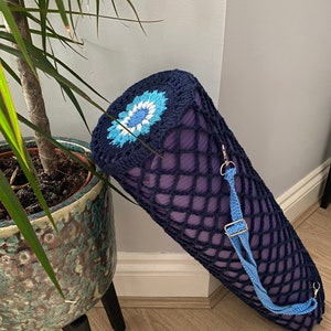 May include: A navy blue crocheted yoga mat carrier with a blue and white flower design. The carrier has a blue adjustable strap.