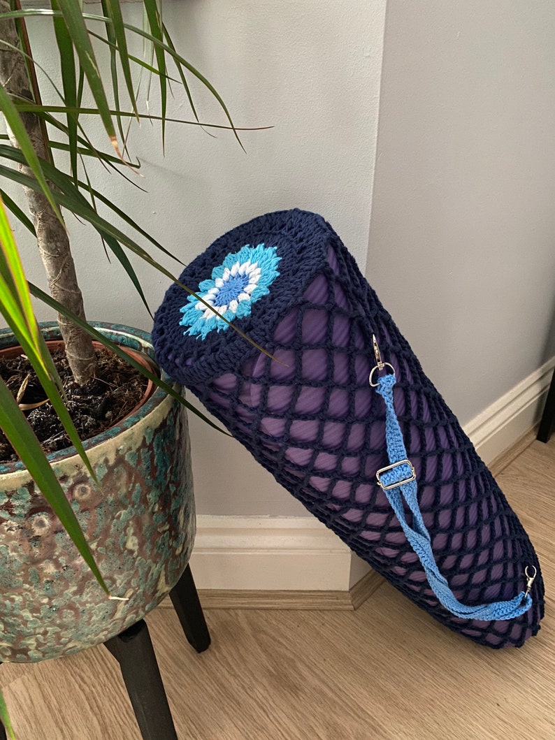 May include: A navy blue crocheted yoga mat carrier with a blue and white flower design. The carrier has a blue adjustable strap.