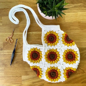 May include: White crochet tote bag with a sunflower pattern in shades of yellow, orange, and brown. The bag has two straps and is made with a granny square stitch.