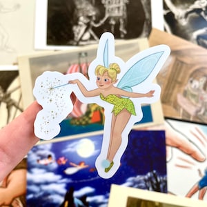 May include: A sticker featuring Tinker Bell, a fairy with green wings and a yellow dress, holding a wand that is sprinkling gold glitter.