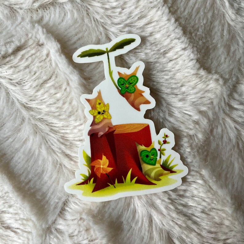 May include: A sticker featuring three cartoon animals with green leaves on their faces. The animals are sitting on a tree stump with a brown base and a green top. The background is a white surface.