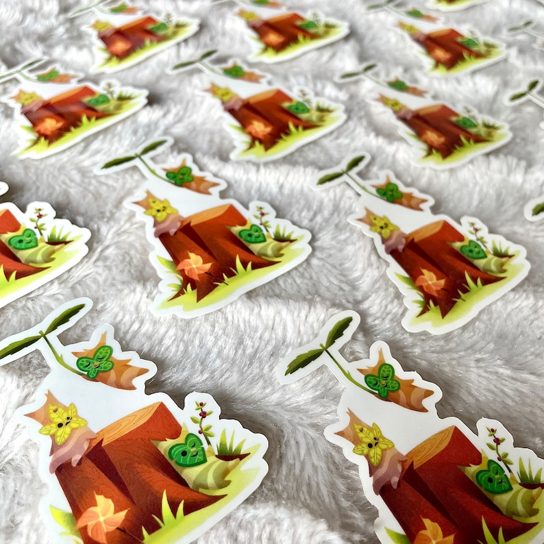 May include: Multiple stickers featuring a cartoon character sitting on a tree stump with a green leaf on its head. The character is surrounded by green leaves and brown leaves. The stickers are on a white fuzzy surface.