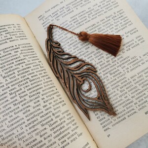 May include: A wooden bookmark shaped like a peacock feather with intricate cutouts. The bookmark has a brown tassel attached to the top.