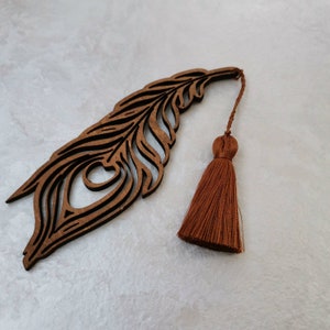 May include: A wooden bookmark shaped like a peacock feather with a brown tassel. The bookmark is intricately carved with details of the feather.