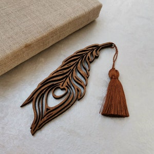 May include: A wooden peacock feather bookmark with a brown tassel. The bookmark is intricately carved with a detailed design.