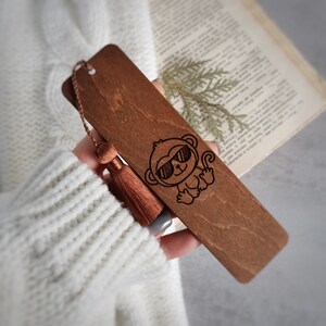 May include: A wooden bookmark with a brown tassel. The bookmark features a laser-engraved illustration of a monkey wearing sunglasses.