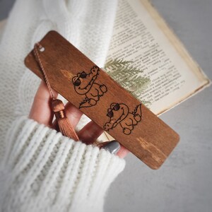 May include: A wooden bookmark with a brown tassel. The bookmark features two cartoon crocodiles wearing sunglasses.