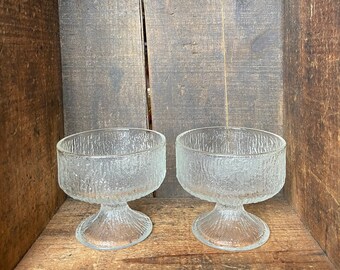May include: Two clear glass dessert bowls with a textured, frosted finish and a pedestal base. The bowls are sitting inside a wooden box.