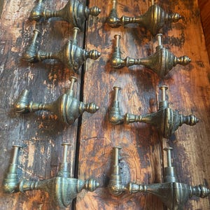 May include: A set of eight antique-style brass drawer pulls arranged in two columns. Each pull features a central spindle-shaped body with decorative detailing and two vertical mounting posts with threaded screws extending from the back.
