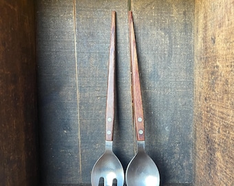 May include: A set of two vintage salad servers with wooden handles. The servers are made of metal and have a silver finish. The handles are a dark brown wood with a smooth finish.