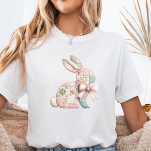 Könnte beinhalten: Weißes T-Shirt mit einem Patchwork-Hasen-Design in Pastelltönen. Der Hase hat Blumen- und geometrische Muster und eine rosa Schleife. Ein lässiges Kleidungsstück für den Alltag.