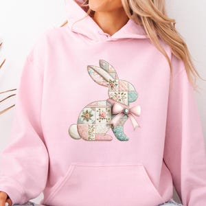 Op de afbeelding: Een lichtroze hoodie met een patchwork konijn ontwerp. Het konijn is versierd met bloemen- en pastelpatronen en een roze strik. De hoodie heeft een kangoeroezak en een capuchon.