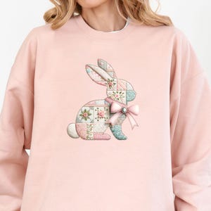 Peut inclure: Un sweat-shirt rose clair orné d'un motif de lapin en patchwork avec des motifs floraux et pastel. Le lapin porte un nœud rose. Le sweat-shirt est de style décontracté et confortable.