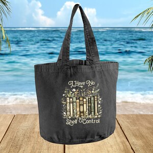 A black tote bag with a printed design on it, featuring a beach scene with palm trees and the ocean in the background.